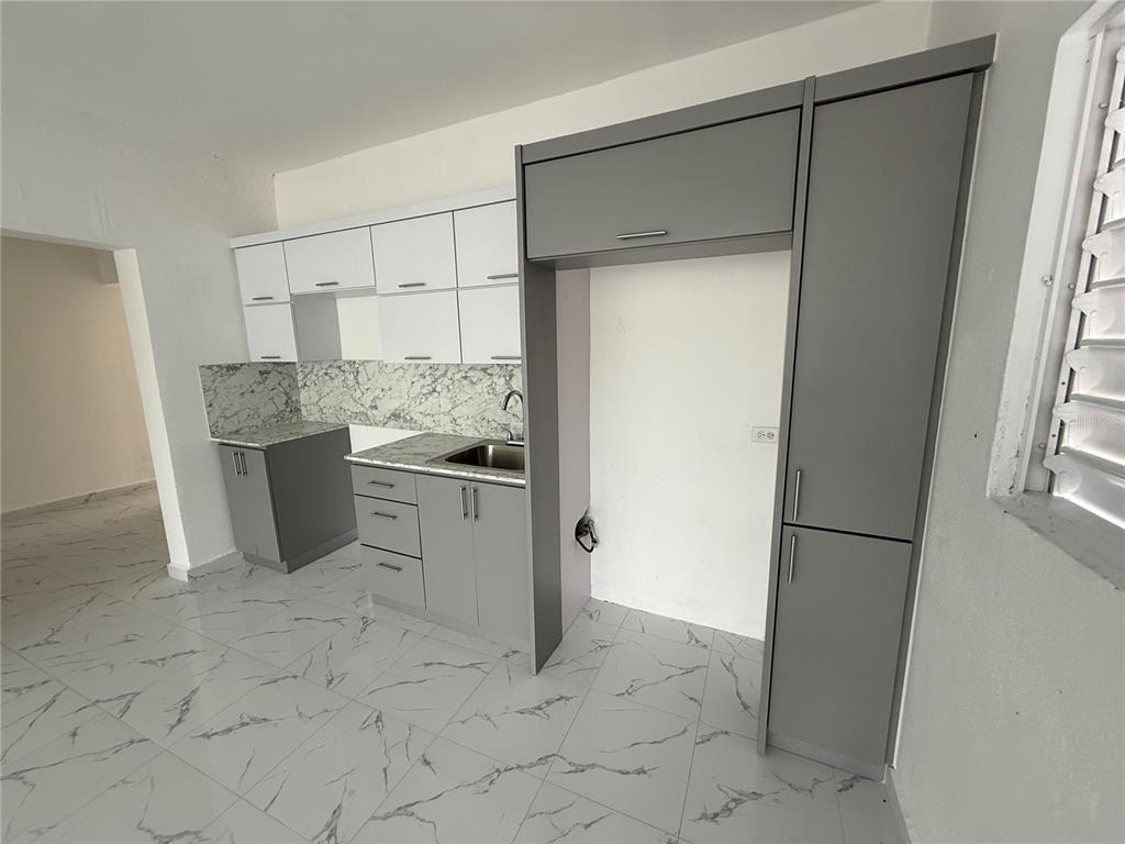 A kitchen features gray and white cabinetry, marble-patterned countertops, and white tile flooring — Zeno Gandia 65 INFANTERÍA, ARECIBO, PR