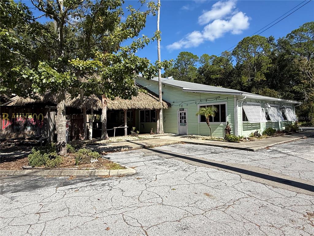 A light green building with a thatched-roof patio area sits beside a cracked asphalt parking lot — 1034 NW 57TH STREET, GAINESVILLE, FL