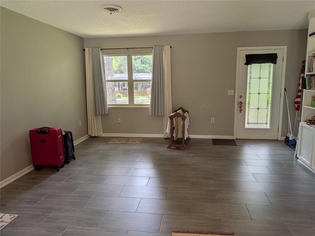 A living room with gray tile flooring, light gray walls, a window, and an entry door — 2720 SE 8TH AVENUE, OCALA, FL