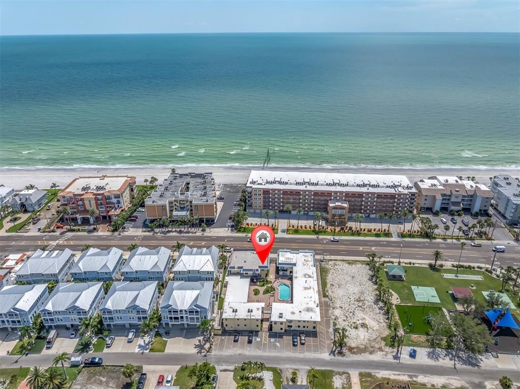 An aerial view shows a beachside resort complex with a pool and nearby oceanfront buildings — 16333 GULF BOULEVARD UNIT 217, ST PETERSBURG, FL
