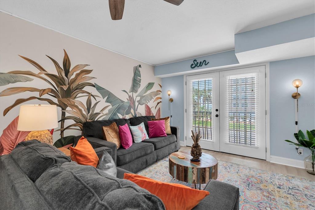 A living room features a large tropical wall mural, a dark sofa, and glass doors — 16333 GULF BOULEVARD UNIT 217, ST PETERSBURG, FL