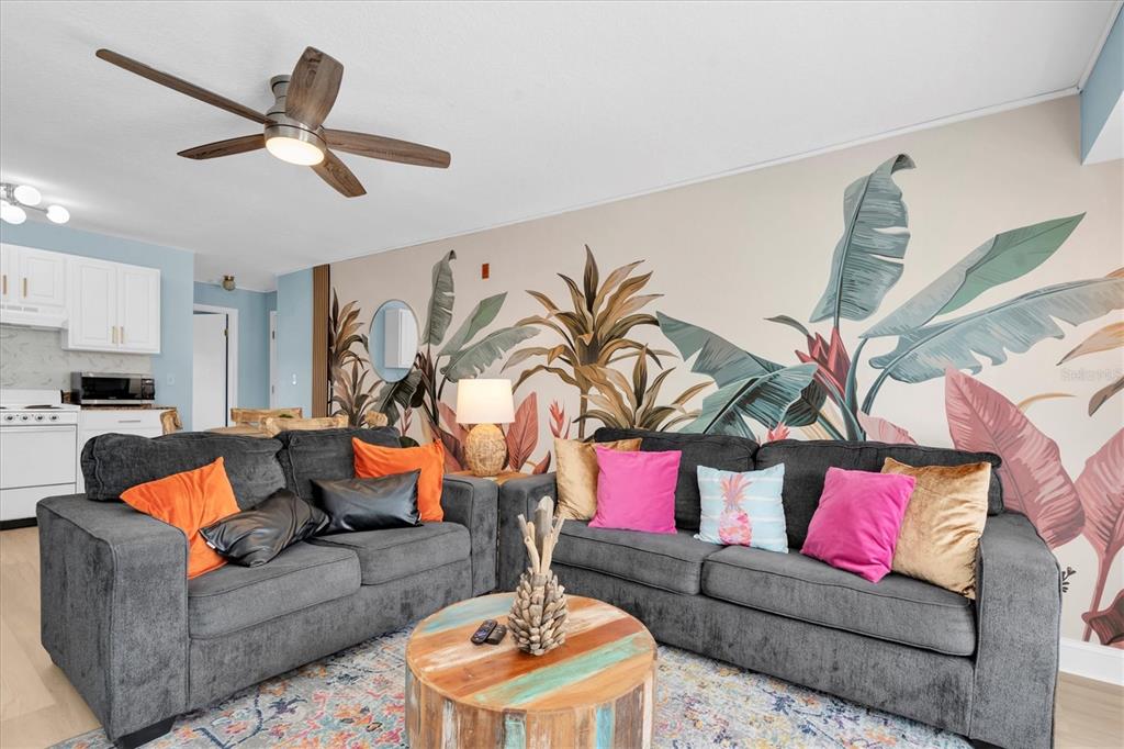 A living room features a grey sectional sofa, a round wooden table, and a tropical mural — 16333 GULF BOULEVARD UNIT 217, ST PETERSBURG, FL