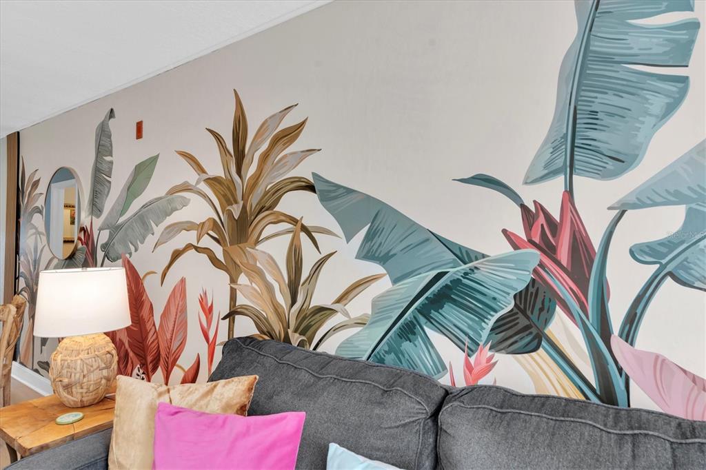 A living room wall features a large tropical leaf mural behind a grey sofa — 16333 GULF BOULEVARD UNIT 217, ST PETERSBURG, FL
