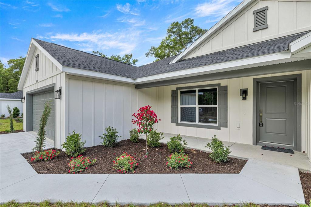 A modern one-story house exterior with white board-and-batten siding, a gray door, and landscaping — 4020 SW 156TH COURT, OCALA, FL