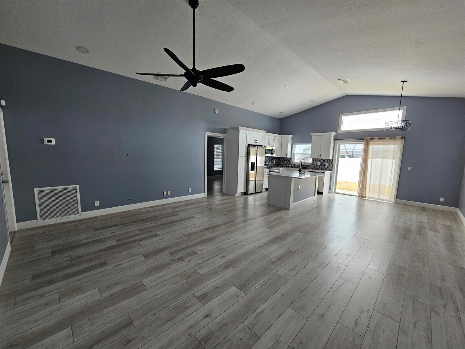 An open-concept living room and kitchen featuring blue walls, light wood-look flooring, and white cabinetry — 6131 Robinson Street, Jupiter FL 33458, JUPITER, FL