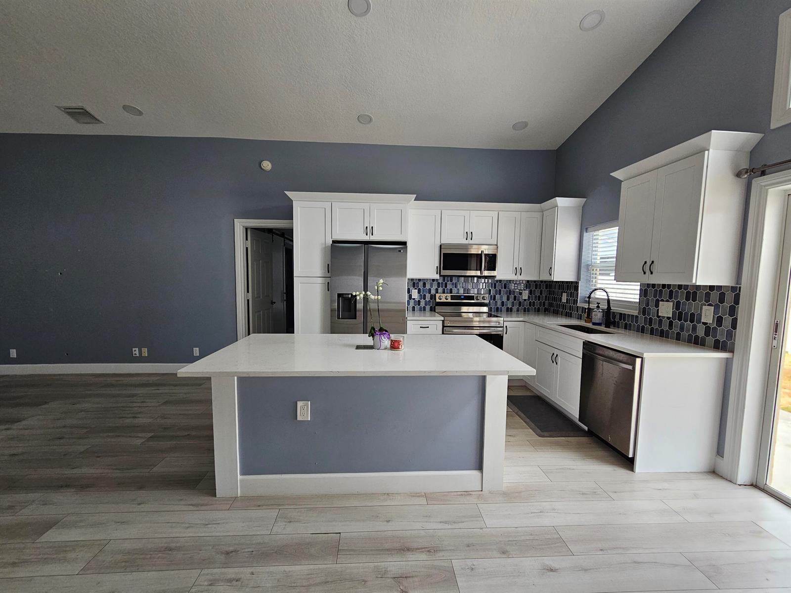 A kitchen features white cabinets, a central island, blue walls, and stainless steel appliances — 6131 Robinson Street, Jupiter FL 33458, JUPITER, FL