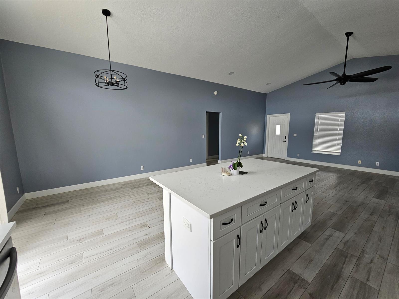 A kitchen island with white cabinets and a quartz countertop sits in a blue room — 6131 Robinson Street, Jupiter FL 33458, JUPITER, FL
