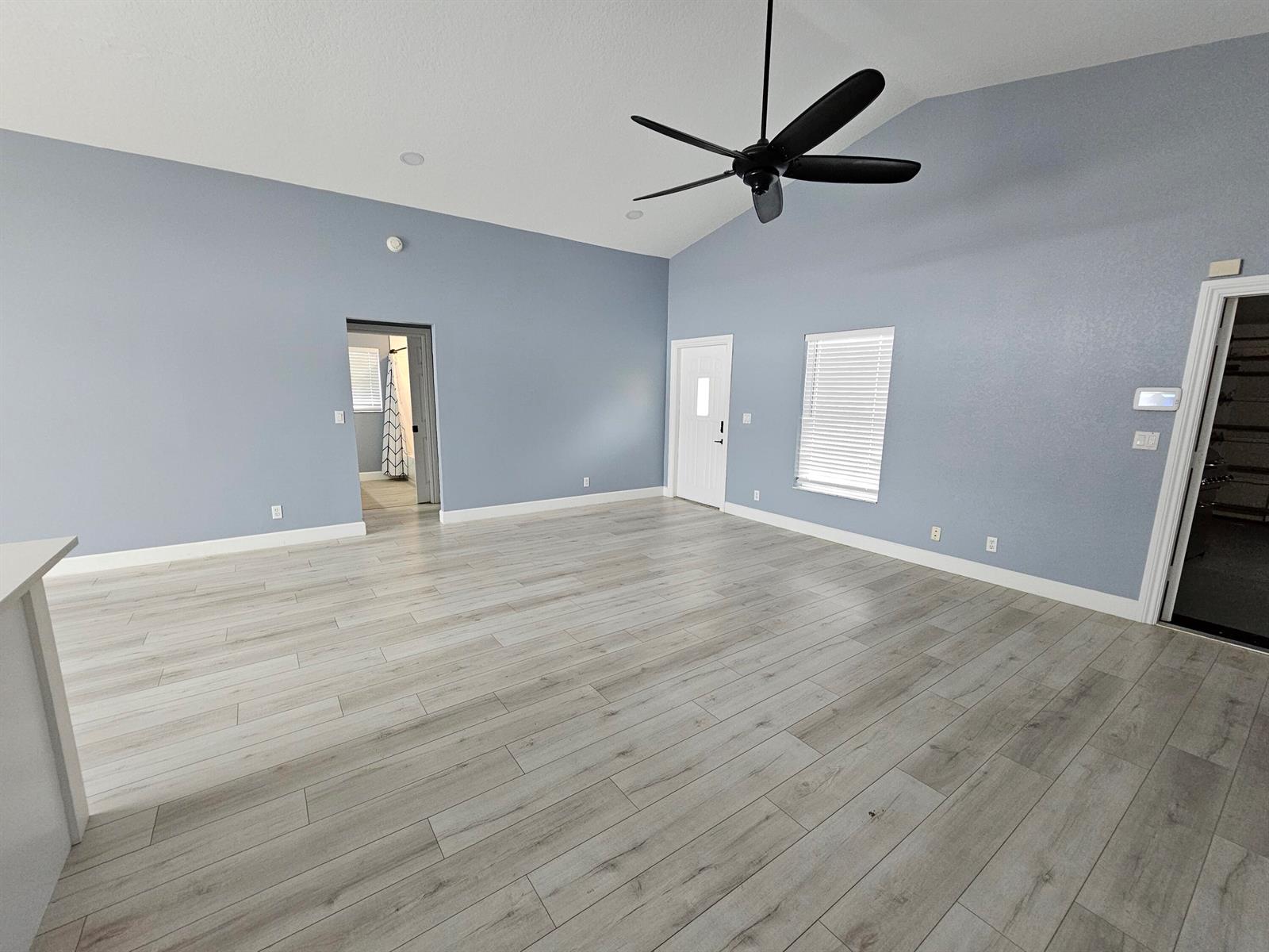 A spacious room with light blue walls, wood-look flooring, a vaulted ceiling, and a fan — 6131 Robinson Street, Jupiter FL 33458, JUPITER, FL