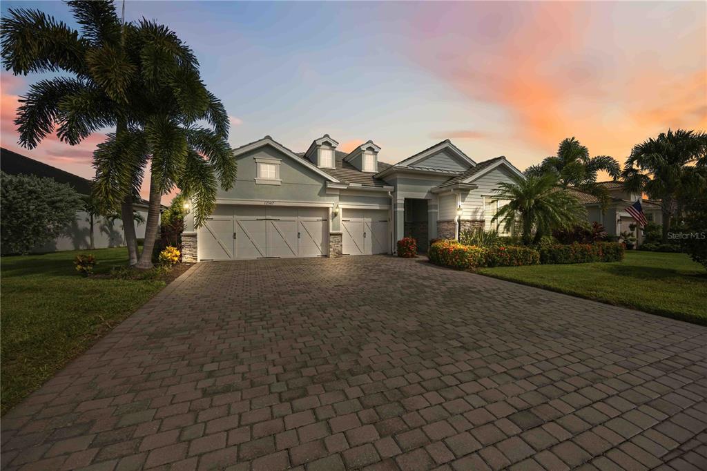 A single-story house with a paved driveway, three-car garage, and palm trees at sunset — 12307 SEABROOK AVENUE, BRADENTON, FL