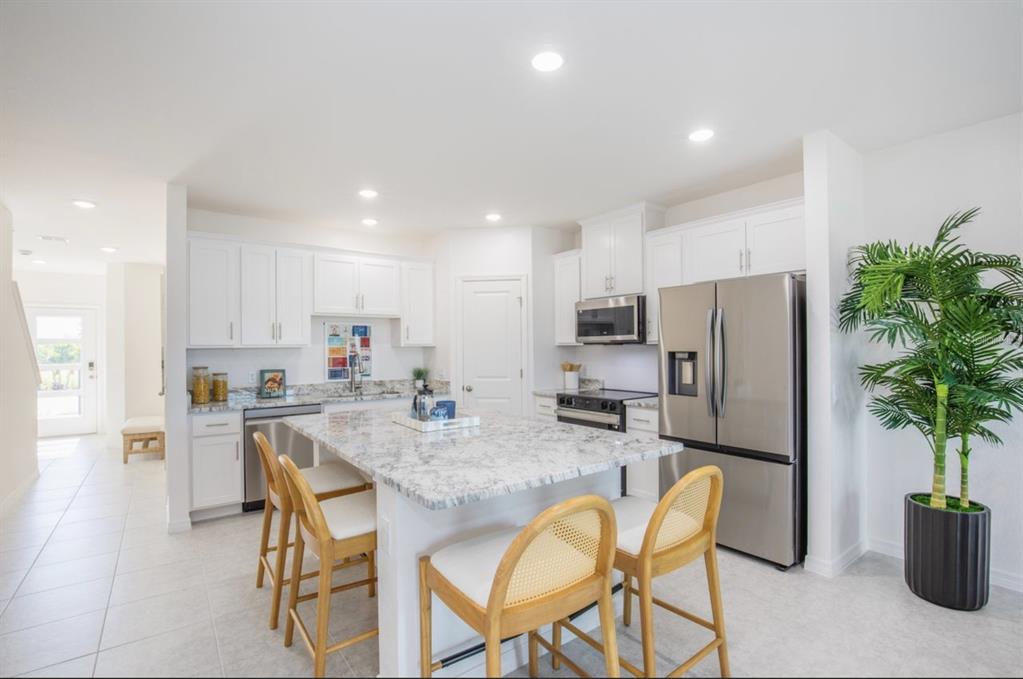 A bright kitchen features white cabinets, granite countertops, a central island, and stainless steel appliances — 10534 FOUNTAIN PALM CIRCLE, BOKEELIA, FL