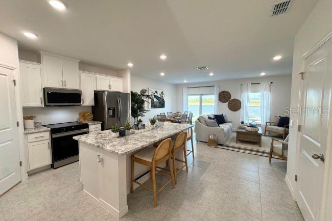 A modern open-concept kitchen with a granite island, stainless appliances, and an adjacent living area — 10534 FOUNTAIN PALM CIRCLE, BOKEELIA, FL