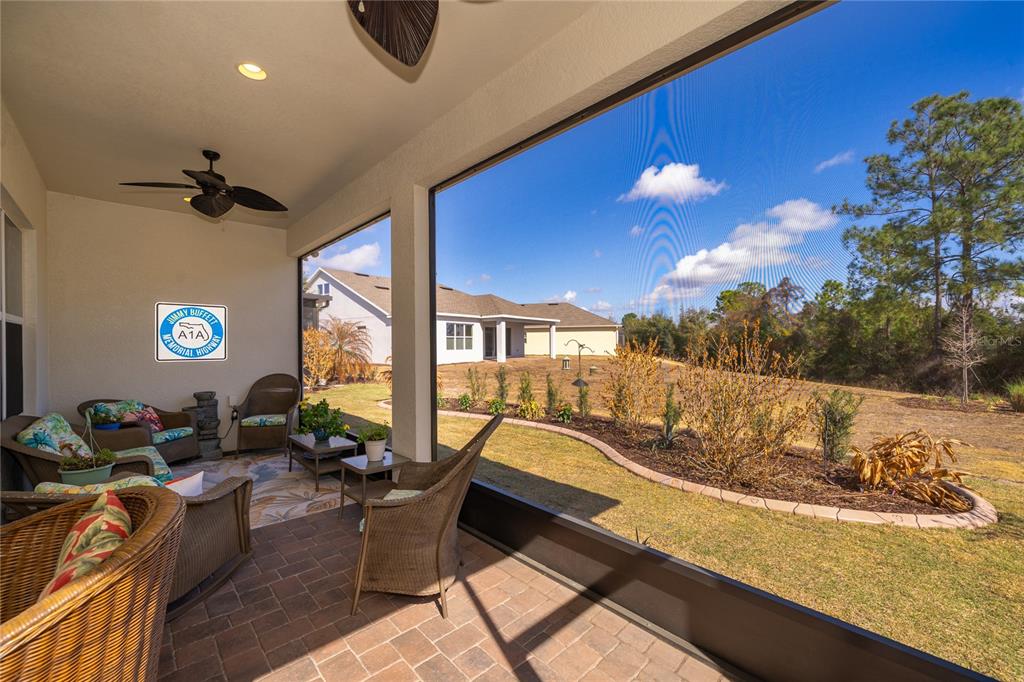 A covered patio with wicker furniture overlooks a grassy backyard and neighboring houses — 7789 FOUR SEASONS BOULEVARD, KISSIMMEE, FL