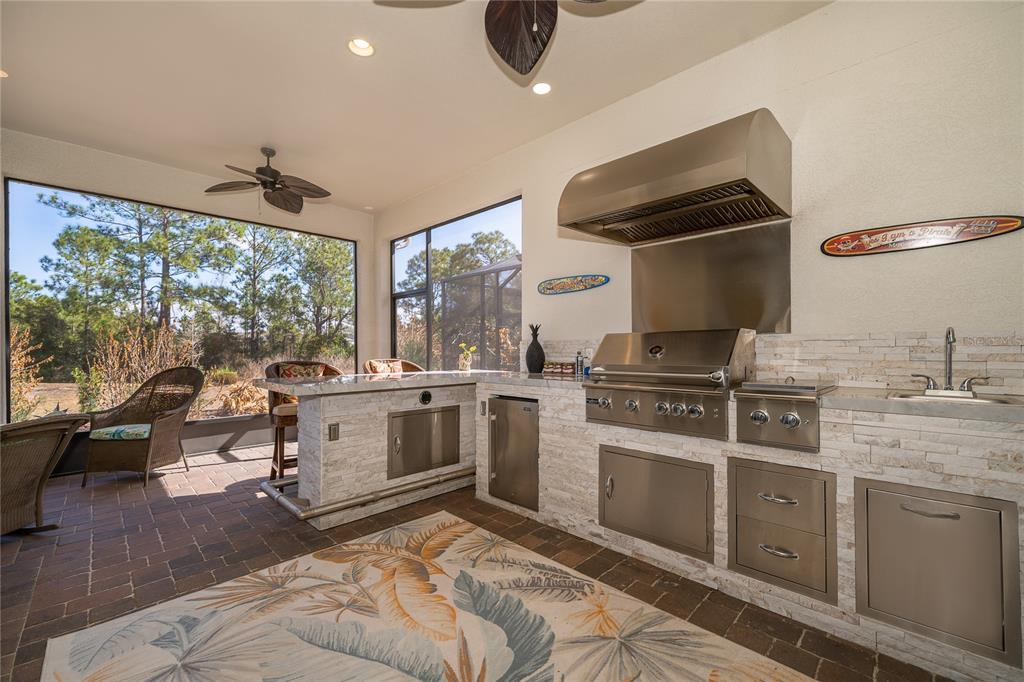 An outdoor kitchen with stone veneer, stainless steel appliances, and a bar area on a patio — 7789 FOUR SEASONS BOULEVARD, KISSIMMEE, FL