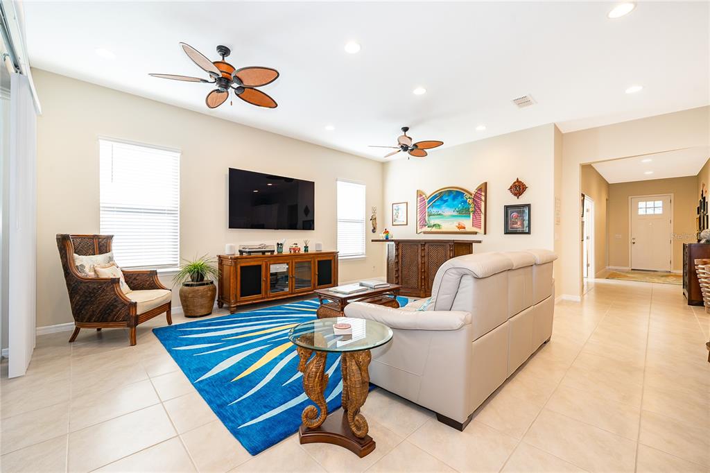 A living room features a blue patterned rug, a beige sofa, and a wooden media console — 7789 FOUR SEASONS BOULEVARD, KISSIMMEE, FL