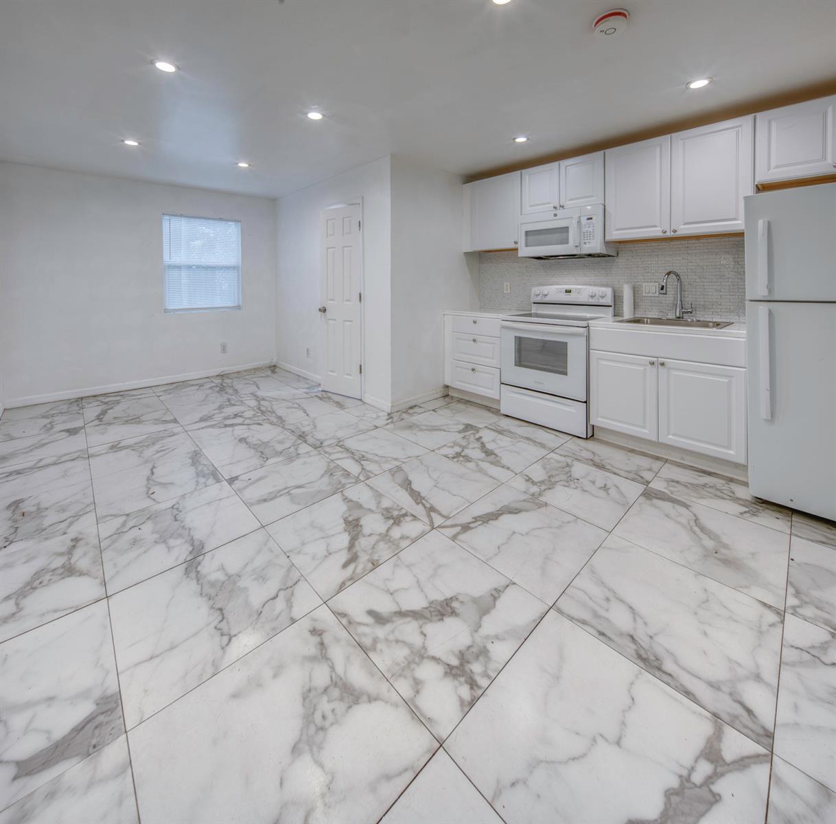 A kitchen features white cabinets, white appliances, and large-format marble-patterned floor tiles — 519 S M Street, FL 33460, FL