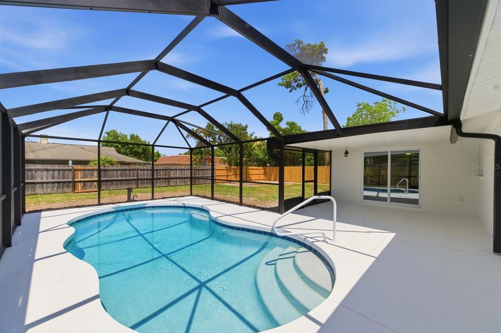 A swimming pool with a white deck is enclosed by a black screen cage — 4760 SEVILLE DRIVE, SARASOTA, FL