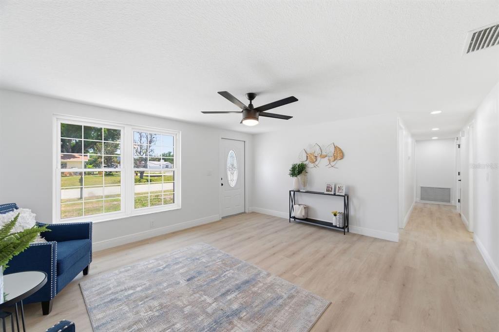 A bright living room features light wood-look flooring, a ceiling fan, and a front door — 4760 SEVILLE DRIVE, SARASOTA, FL