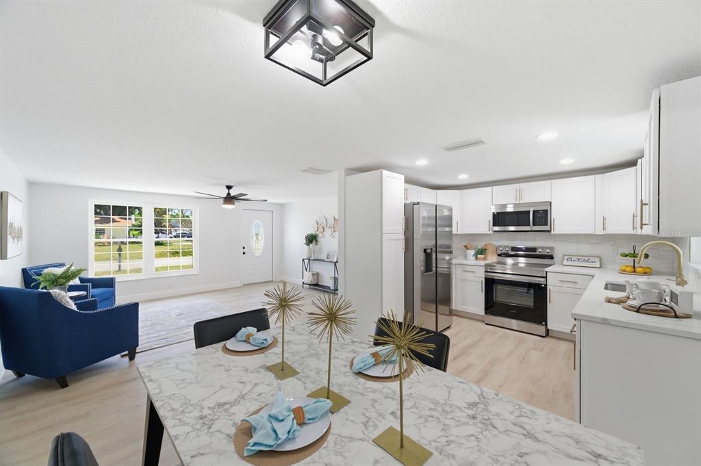 A bright, open-concept kitchen and dining area with white cabinets, stainless appliances, and light flooring — 4760 SEVILLE DRIVE, SARASOTA, FL