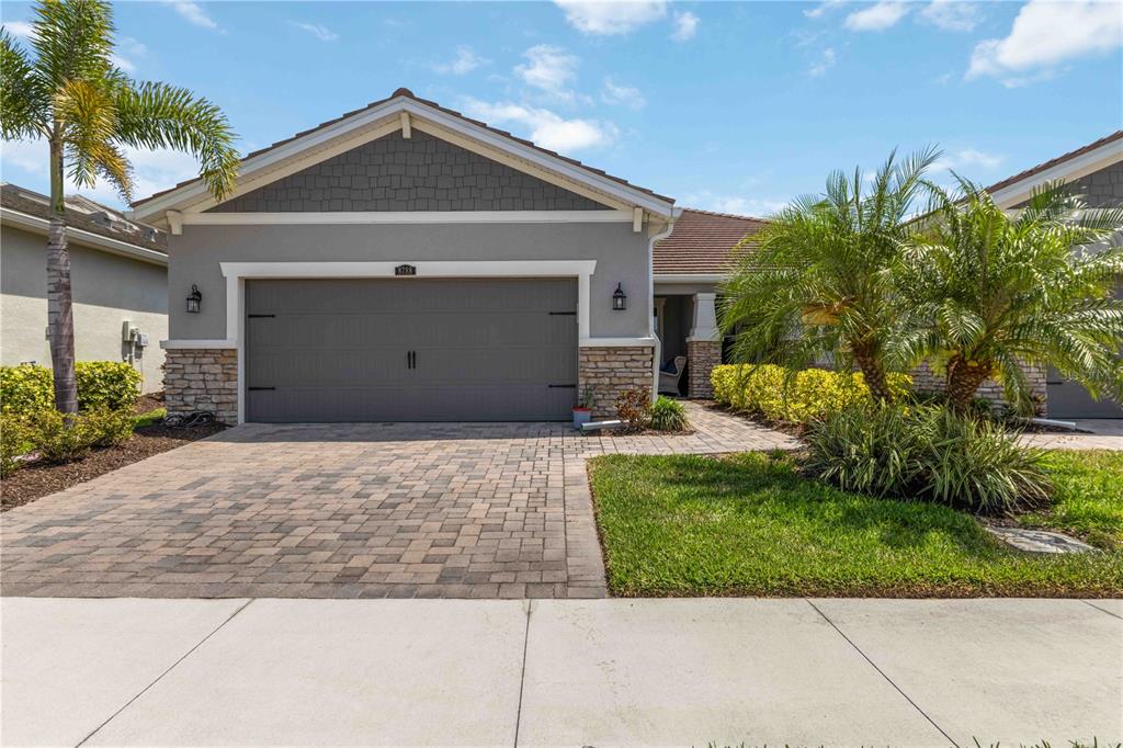 A single-story house with a gray garage, stone accents, and palm trees in the front yard — 8788 RAIN SONG ROAD UNIT 384, SARASOTA, FL