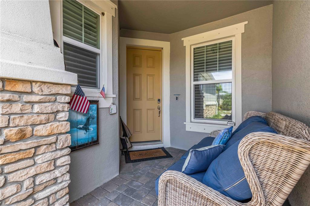 A covered front porch features a tan door, stone pillar, and a wicker loveseat — 8788 RAIN SONG ROAD UNIT 384, SARASOTA, FL