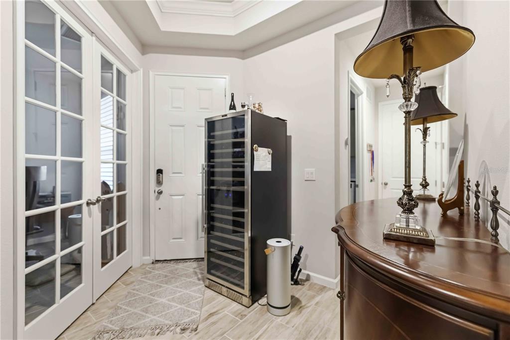 An entryway features a wine cooler, a wooden console table with a lamp, and French doors — 8788 RAIN SONG ROAD UNIT 384, SARASOTA, FL