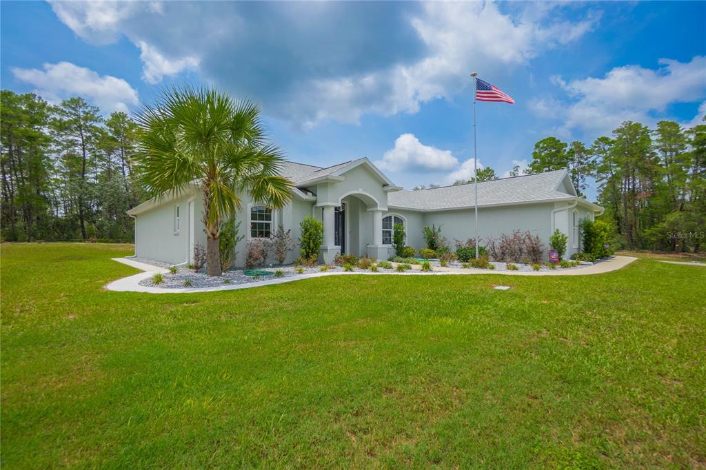 A light-colored single-story house with a palm tree and an American flag in the yard — 4136 W FINDLAY STREET, CITRUS SPRINGS, FL
