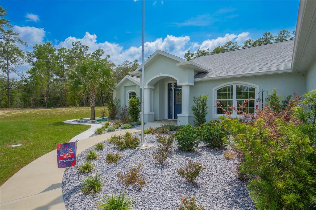 A light-colored house exterior features a front walkway, a flagpole, and a landscaped rock garden — 4136 W FINDLAY STREET, CITRUS SPRINGS, FL