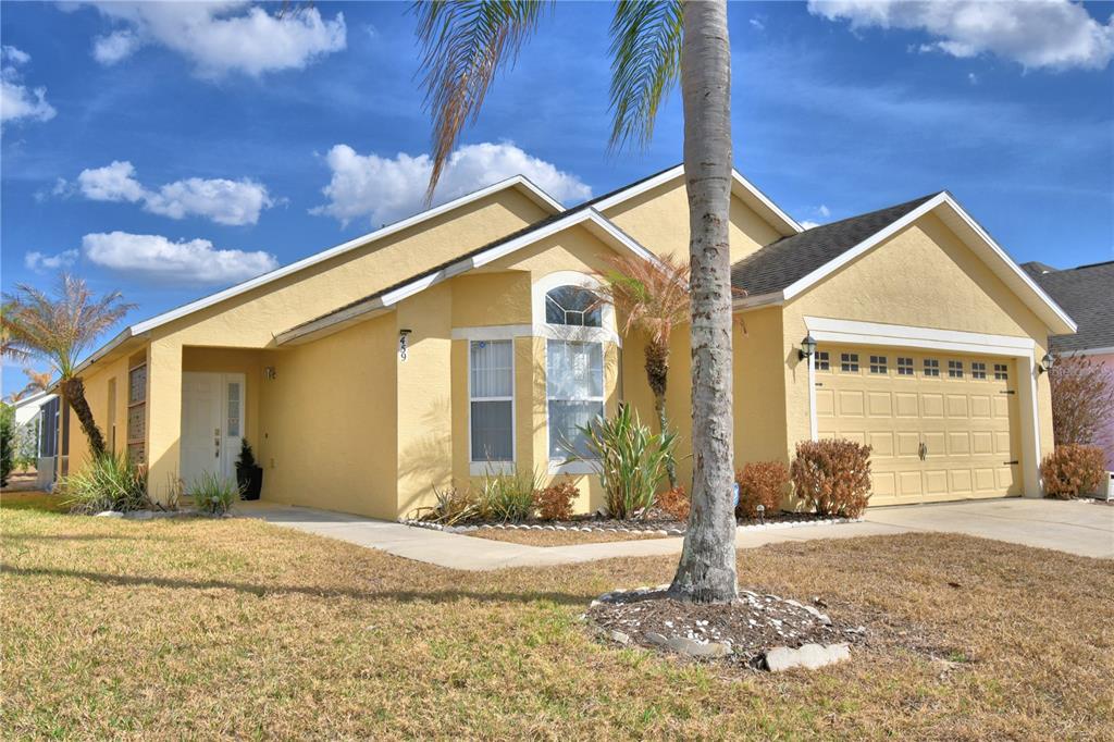 A yellow single-story house with a two-car garage and a palm tree in the yard — 459 TIVOLI CIRCLE, DAVENPORT, FL