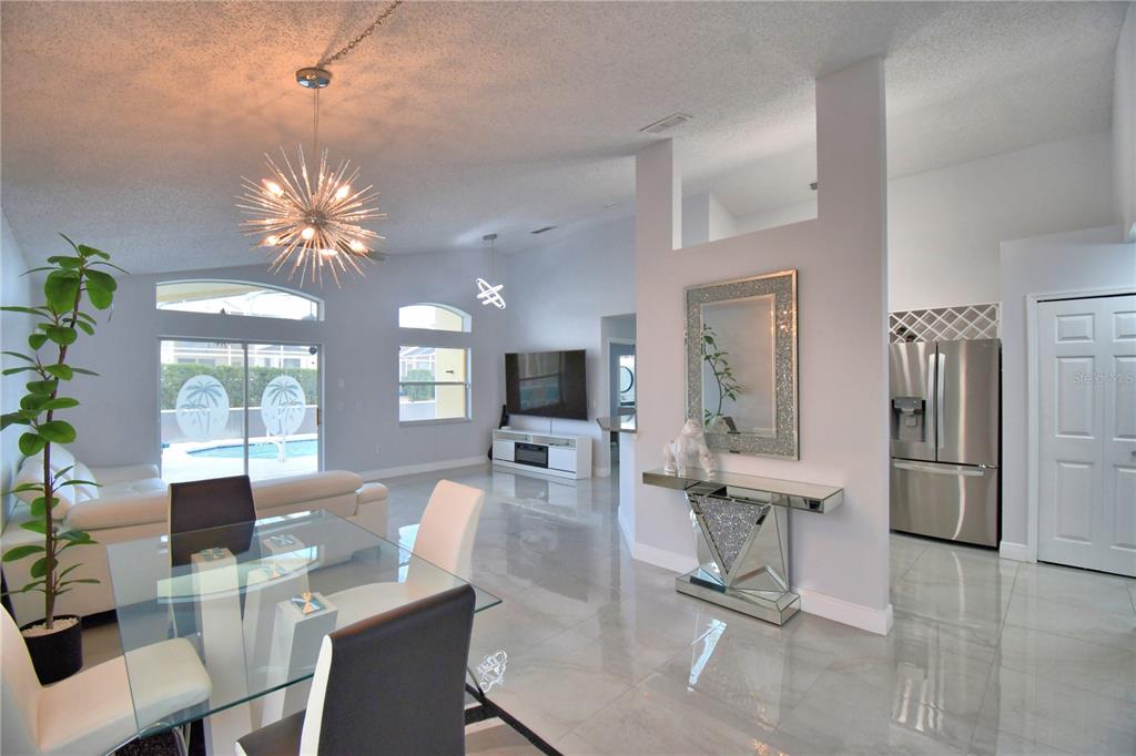 A bright, open-concept living and dining area features white tile floors and a modern chandelier — 459 TIVOLI CIRCLE, DAVENPORT, FL