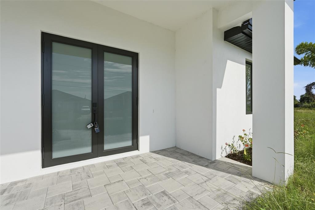 A covered patio with light-colored pavers and a dark-framed double glass door — 8472 AGATE STREET, PORT CHARLOTTE, FL