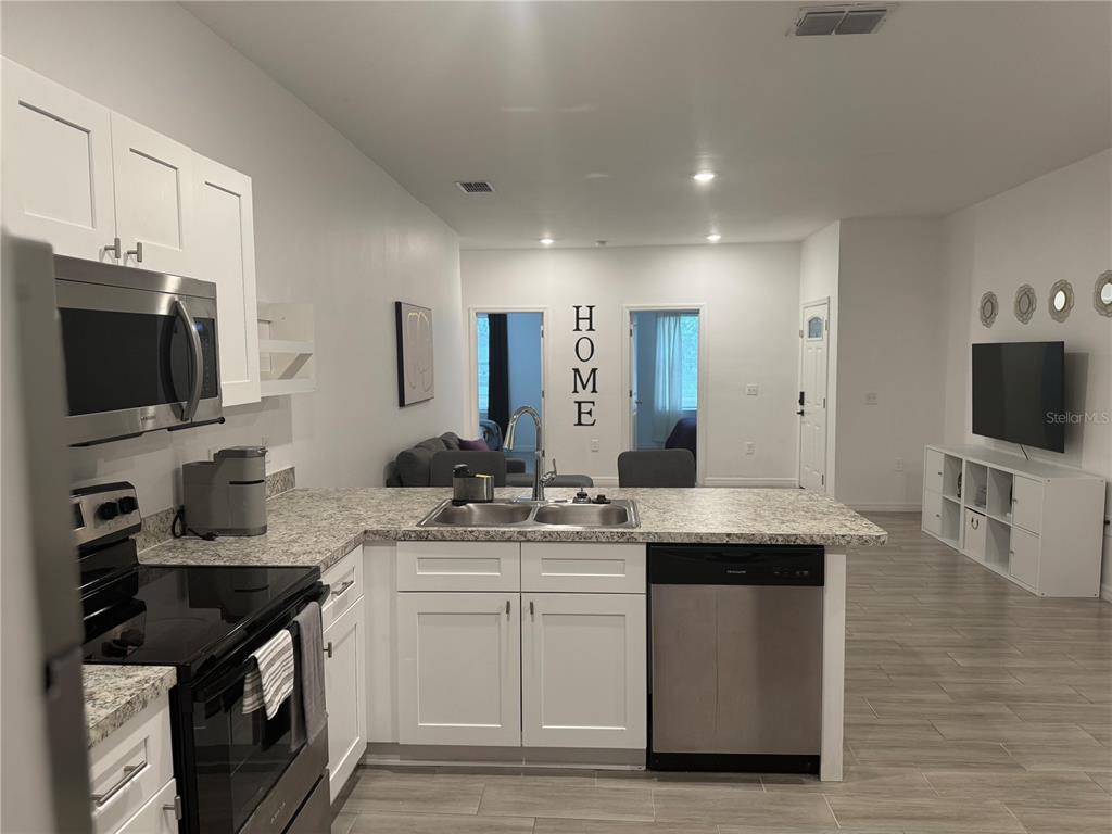 A kitchen with white cabinets and granite countertops overlooks a living area with tile flooring — 699 W KALEY STREET, ORLANDO, FL