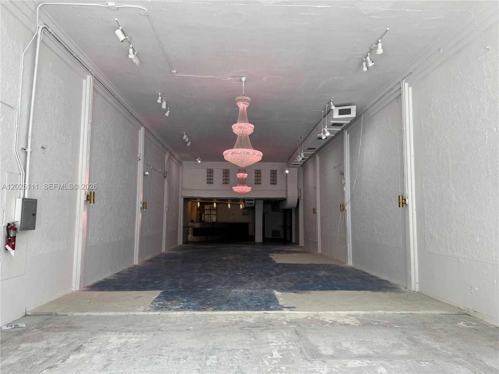 An empty commercial space features white walls, a large tiered chandelier, and exposed concrete flooring — 1929 Hollywood Blvd, Hollywood FL 33020, HOLLYWOOD, FL