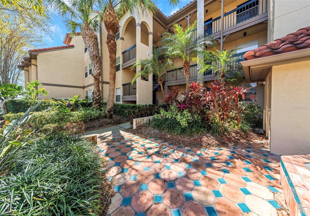A paved walkway leads to the entrance of a multi-story apartment building with palm trees — 2400 FEATHER SOUND DRIVE UNIT 412, CLEARWATER, FL