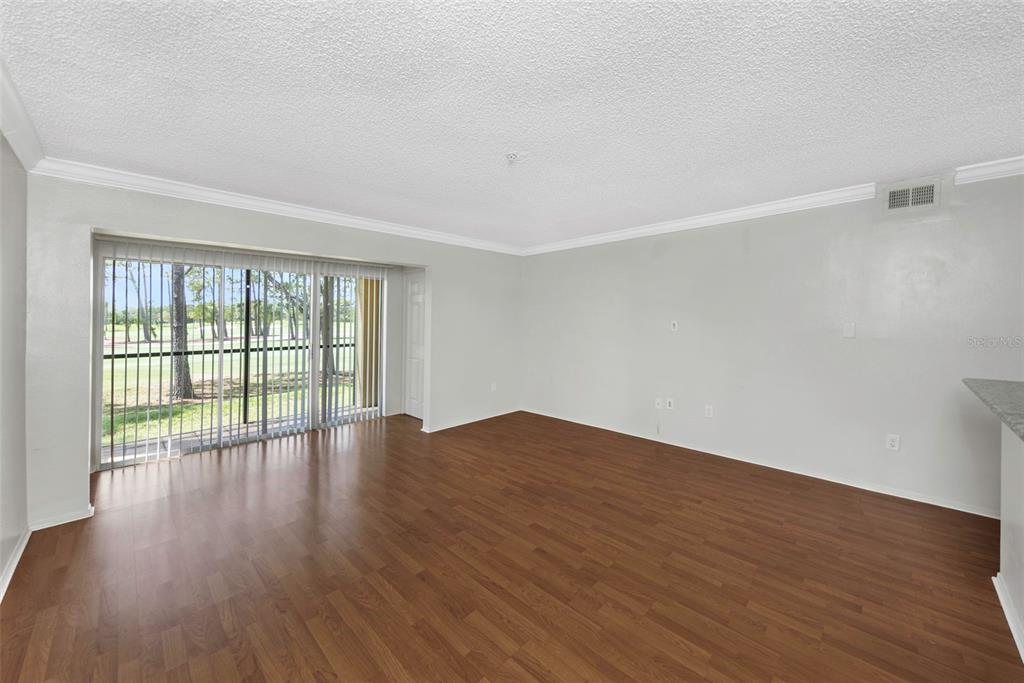 An empty living room features wood-look flooring, light gray walls, and sliding glass patio doors — 2400 FEATHER SOUND DRIVE UNIT 412, CLEARWATER, FL
