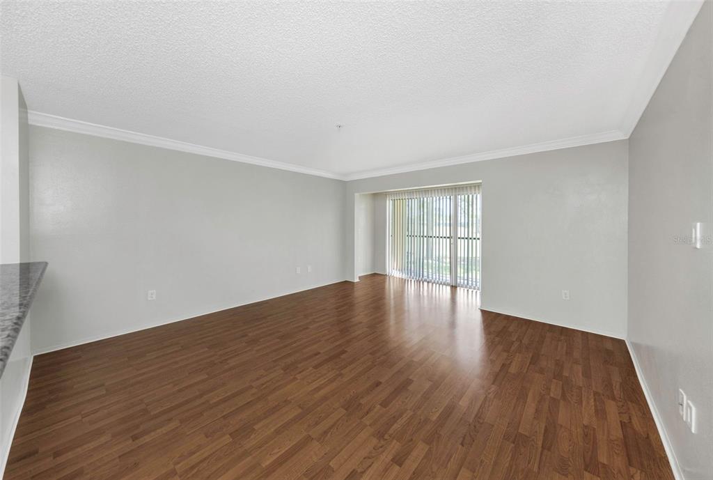An empty living room with wood-look flooring, light gray walls, and a sliding glass door — 2400 FEATHER SOUND DRIVE UNIT 412, CLEARWATER, FL