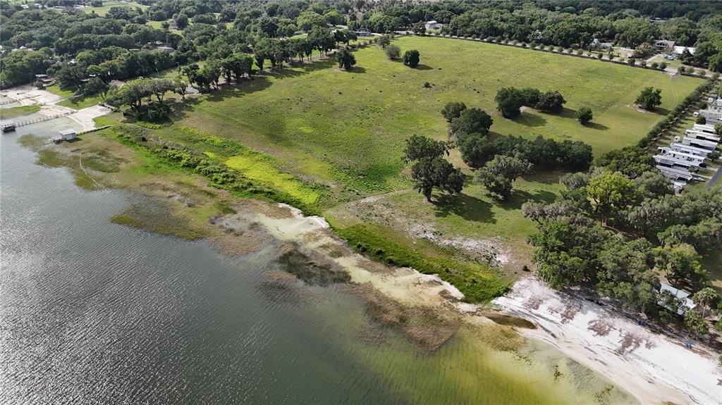 An aerial view shows a large grassy field bordering a lake with a sandy shoreline — TBD SE SUNSET HARBOR ROAD, WEIRSDALE, FL
