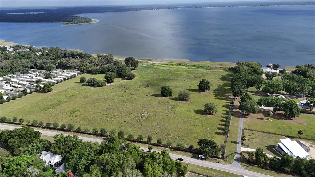 An aerial view shows a large, grassy vacant lot bordering a lake and a road — TBD SE SUNSET HARBOR ROAD, WEIRSDALE, FL