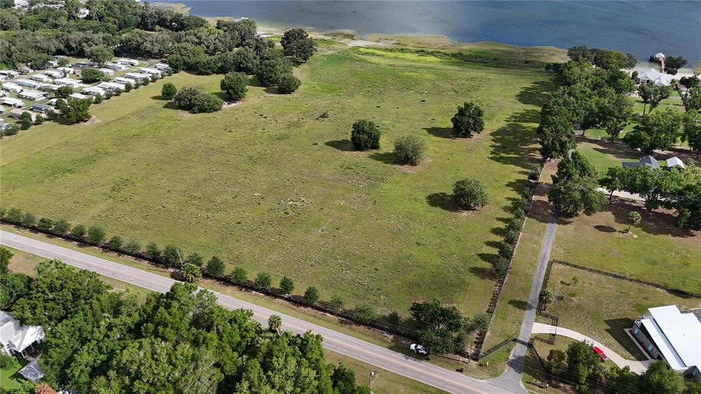 An aerial view shows a large, grassy vacant lot bordered by a road and trees — TBD SE SUNSET HARBOR ROAD, WEIRSDALE, FL