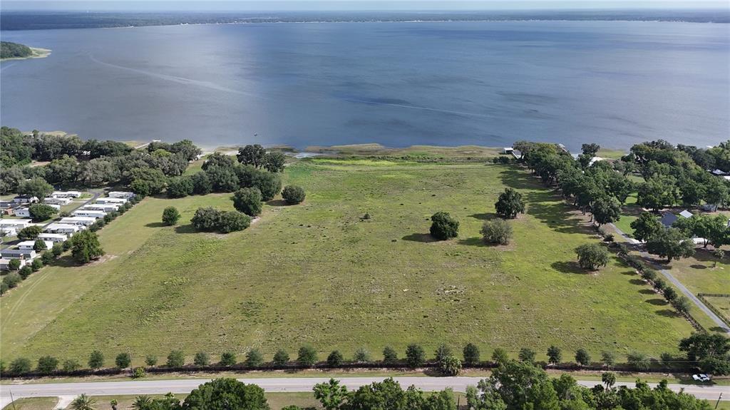 An aerial view shows a large, grassy vacant lot bordering a lake — TBD SE SUNSET HARBOR ROAD, WEIRSDALE, FL