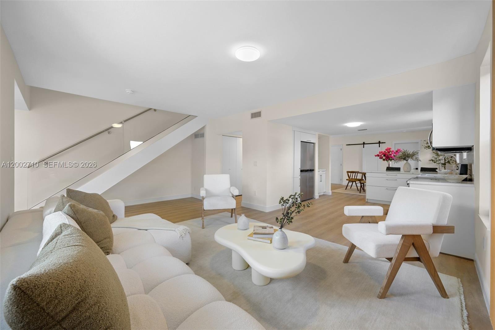 A bright living room features a white sectional sofa, modern coffee table, and open kitchen — 7996 Crespi Blvd, Miami Beach FL 33141, MIAMI BEACH, FL
