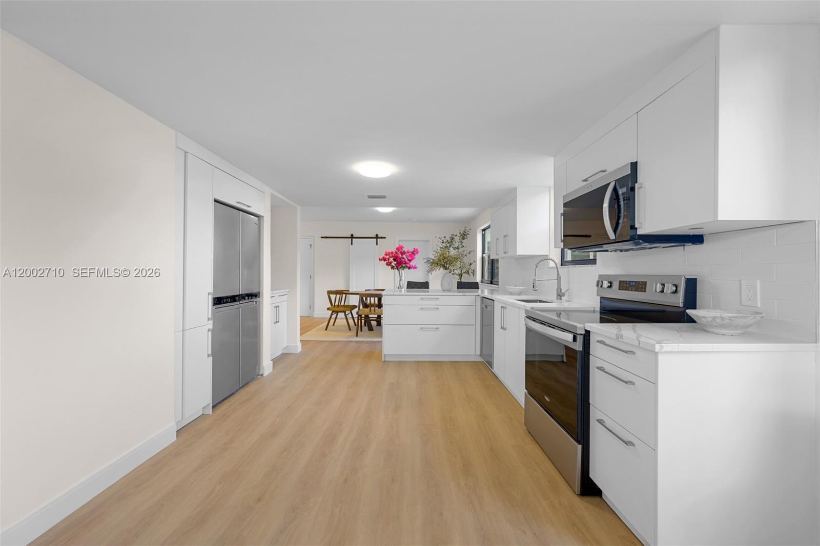 A modern kitchen features white cabinetry, stainless steel appliances, and light wood-look flooring — 7996 Crespi Blvd, Miami Beach FL 33141, MIAMI BEACH, FL