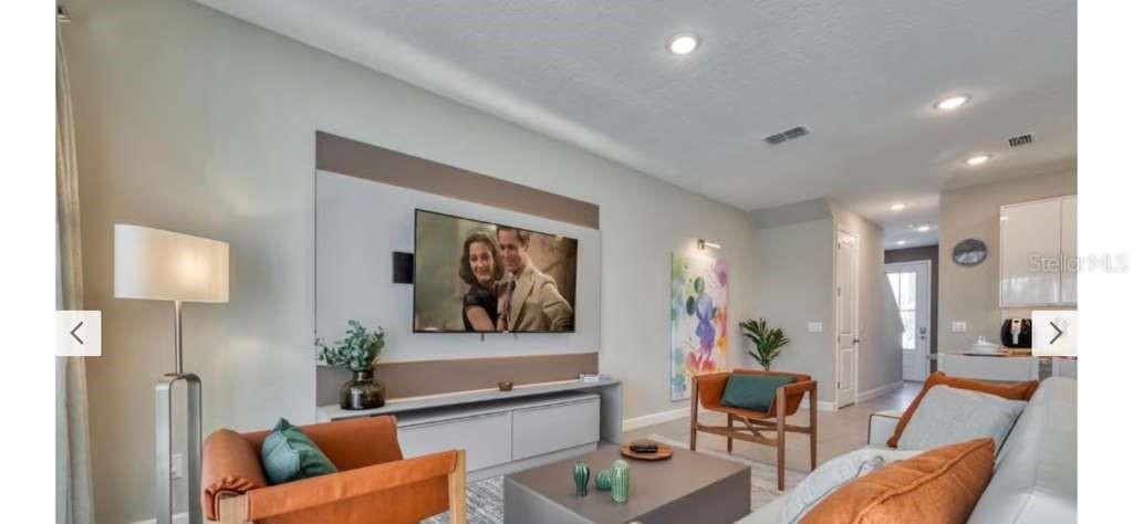 A modern living room features a wall-mounted television, a low media console, and orange armchairs — 8001 FORMOSA VALLEY, KISSIMMEE, FL