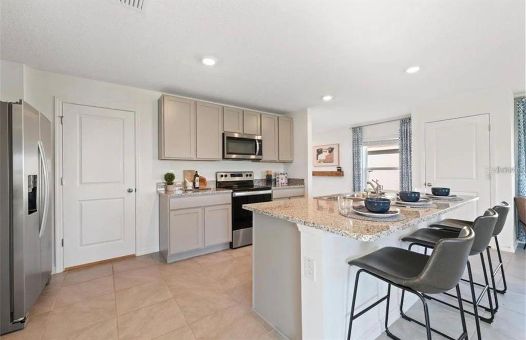 A kitchen with light gray cabinets, granite countertops, a center island, and stainless steel appliances — 16716 GLACIER BAY LOOP, WIMAUMA, FL