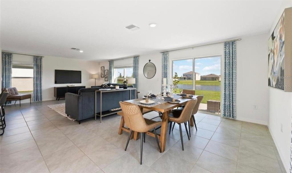 An open-concept living and dining area features tile flooring, a sliding glass door, and furniture — 16716 GLACIER BAY LOOP, WIMAUMA, FL