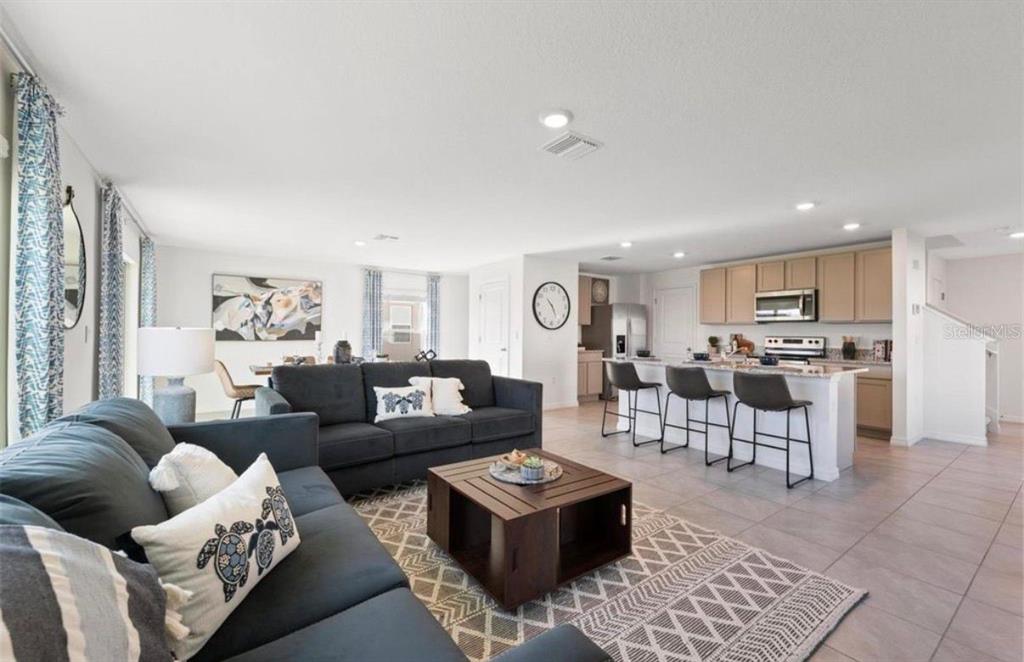 An open-concept living room and kitchen featuring gray sofas, a coffee table, and bar seating — 16716 GLACIER BAY LOOP, WIMAUMA, FL