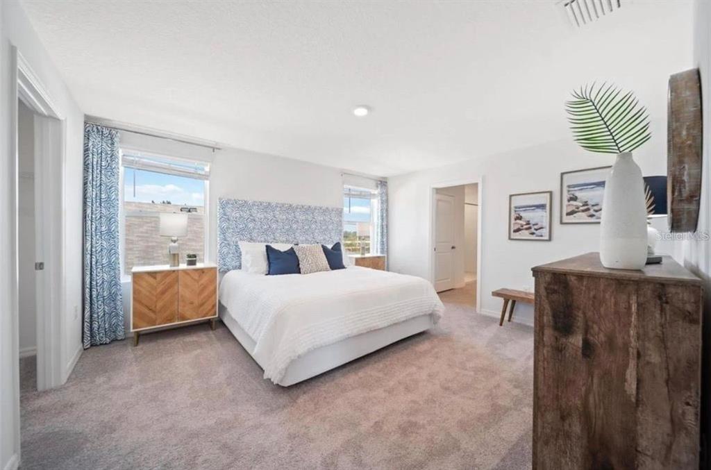 A bedroom features a king bed with a patterned headboard, two windows, and carpeted flooring — 16716 GLACIER BAY LOOP, WIMAUMA, FL