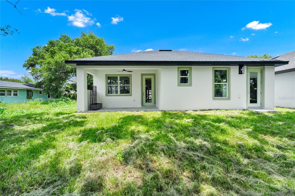 The back exterior of a white house features a covered patio and green-trimmed windows — 2034 E GRANT AVENUE, ORLANDO, FL