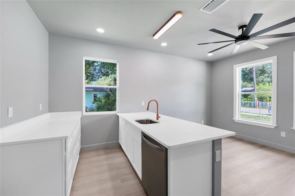A modern kitchen features white cabinetry, quartz countertops, a central island, and light wood flooring — 2034 E GRANT AVENUE, ORLANDO, FL