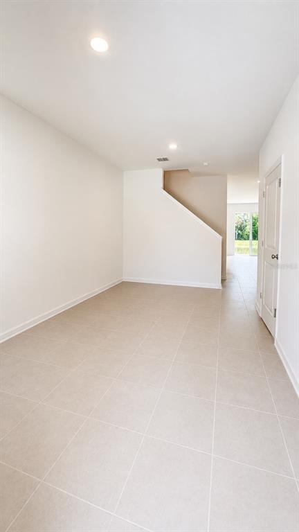 A bright, empty room with beige tile flooring and a staircase leading to the upper level — 3045 CHROMATIC STREET, KISSIMMEE, FL