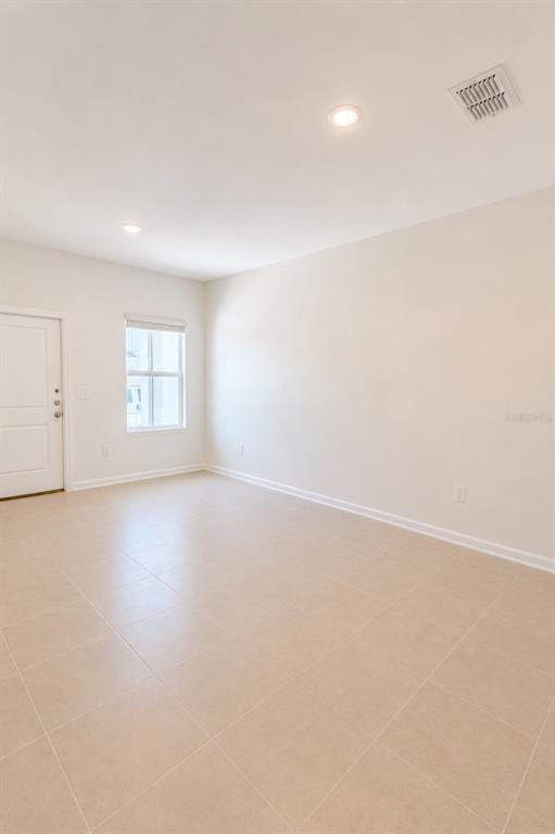 An empty room features beige tile flooring, white walls, a single window, and a door — 3045 CHROMATIC STREET, KISSIMMEE, FL